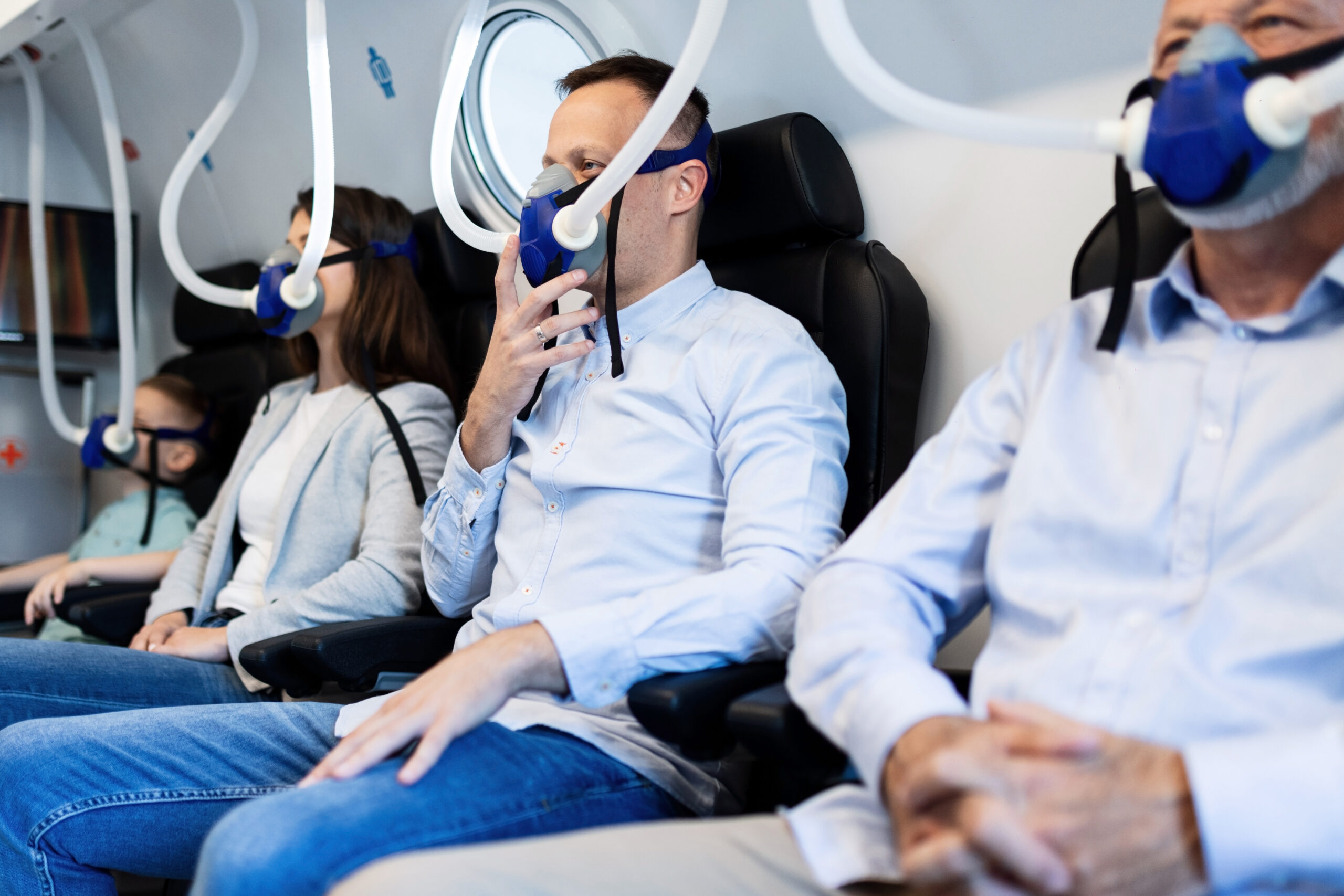 Group of people breathing through oxygen masks in hyperbaric chamber. Focus is on mid adult man.